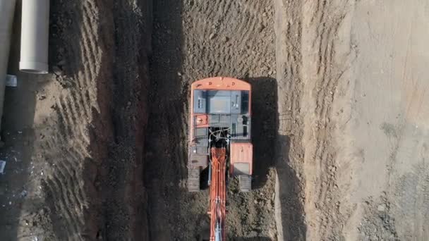 Luftaufnahme eines orangefarbenen oder roten Baggerfahrzeugs, das den Sandboden zur Verlegung von Wasserleitungen in das nationale Infrastruktursystem gräbt. Arbeitsplatzprojekt im Außenbereich — Stockvideo
