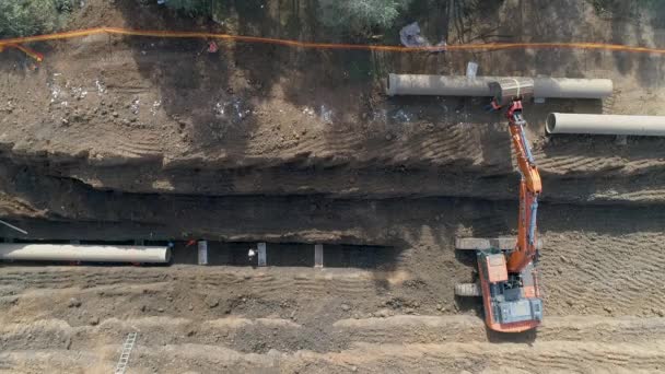 Luftaufnahme eines orangefarbenen oder roten Baggerfahrzeugs, das den Sandboden zur Verlegung von Wasserleitungen in das nationale Infrastruktursystem gräbt. Arbeitsplatzprojekt im Außenbereich — Stockvideo