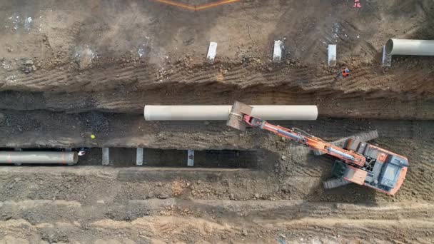 Instalación de tubos de hormigón. Aérea por encima de los hombres en el trabajo exterior con maquinaria pesada para conectar e instalar tuberías de agua o alcantarillado en un terreno de excavación — Vídeos de Stock