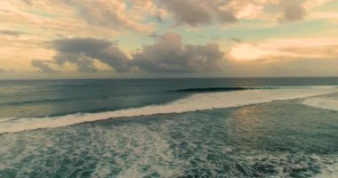 Aerial drone shot over clear sea ocean water at sunset. Low attitude shot over surfers catching waves as lifestyle activity