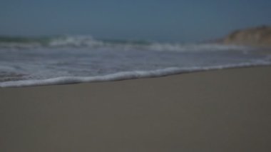 Dalgalar ve deniz köpüğü ile deniz kıyısının düşük açılı görüntüsü ve yavaş çekim görüntüsü.