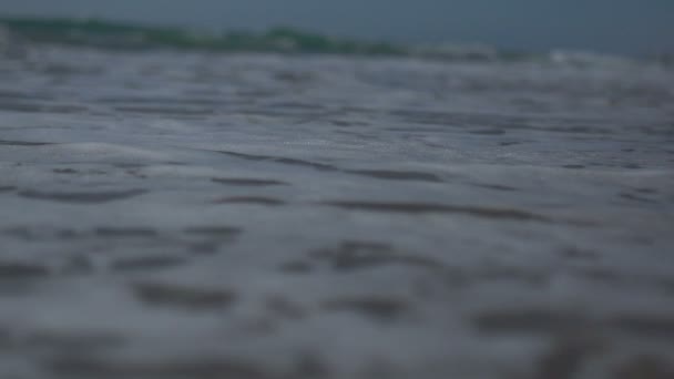Dalgalar ve deniz köpüğü ile deniz kıyısının düşük açılı görüntüsü ve yavaş çekim görüntüsü. — Stok video