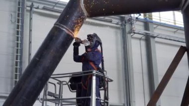 Koruyucu maskeli ve takım elbiseli profesyonel ağır endüstri işçisi fabrikada metal yapımında çalışıyor. Çelik ve demir kaynaklama şantiyesi. Kaynak makinesi kıvılcımlar ve parıltılarla.