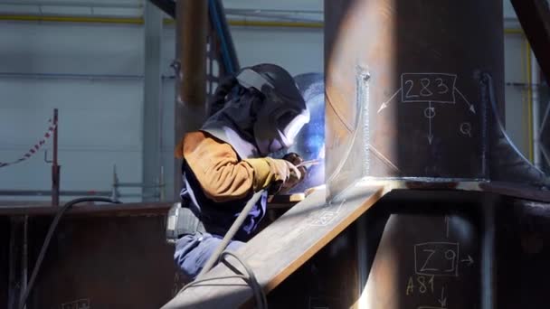 Profesionální pracovník v těžkém průmyslu svářeč v ochranné masce a oblek pracuje s kovovou konstrukcí na továrně. Stavba ocelových a železných svařovacích zařízení. Svařovací stroj s jiskry a záblesky.
