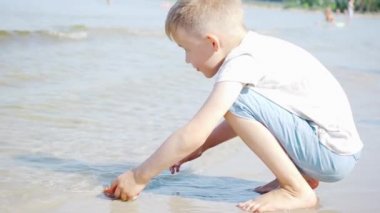 Akıllı küçük çocuk güneşli bir günde kumsalda suda oynuyor. Slow Motion çekimi. Aile Kavramı, Arkadaşlık, Eğitim, Keşif, Tatil, Yeni Hayat ve Aşk. 