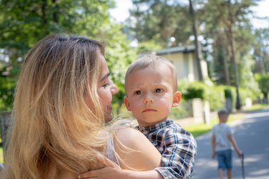 Oğlunu kucaklayan güzel bir anne. Sevimli anne çocuğunu kucaklıyor ve mahallede yürürken ona bakıyor. Aile kavramı.