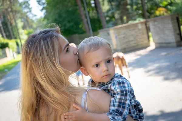 Oğlunu kucaklayan güzel bir anne. Sevimli anne çocuğunu kucaklıyor ve mahallede yürürken ona bakıyor. Aile kavramı.