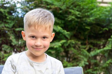 Gülümseyen ve kameraya bakan sevimli çocuk portresi. Güneşli bir günde, dişlek bir gülümsemeyle mutlu, yakışıklı bir çocuk..