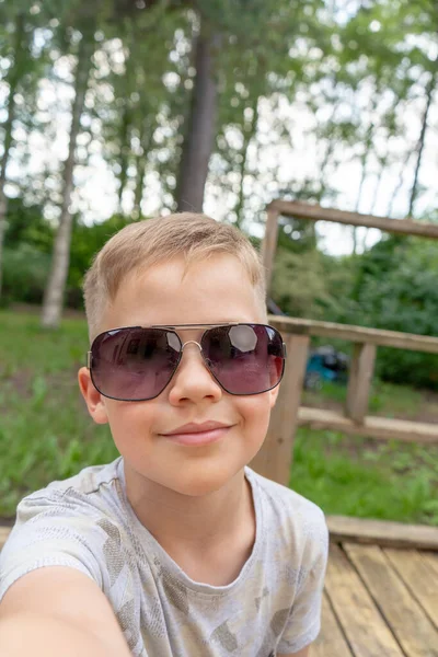 Gözlüklü, selfie çeken küçük bir çocuk. Gülümseyen sevimli çocuk fotoğraf çekiyor ve ailesiyle sohbet ediyor. Dikey fotoğraf.