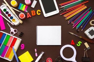 Farklı kırtasiye malzemeleri, okul not defteri çalar saati ve kahverengi arka planda malzemeler. Okul konseptine geri dönelim. Sancak biçimi. Üst görünüm