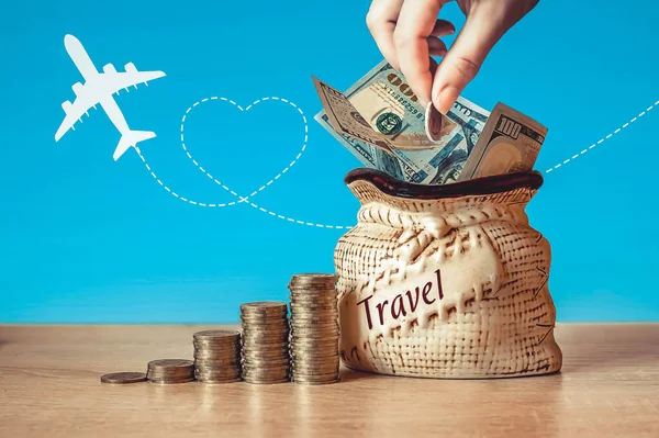 コイン付きバッグの米ドル紙幣テーブルの上にスタック 飛行機のシルエットと青の背景 旅行でお金を節約する概念 — ストック写真