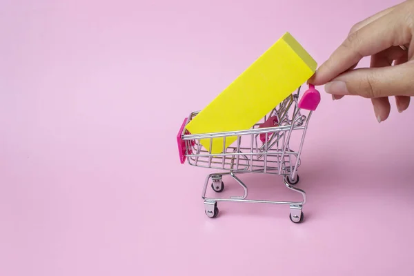 女性の手の閉じるピンクの背景に内側に赤いプラスチックハンドルと黄色のボックスとおもちゃの金属ショッピングカートをプッシュします 大規模な販売と食料品の割引 食料品のための最高の価格 — ストック写真