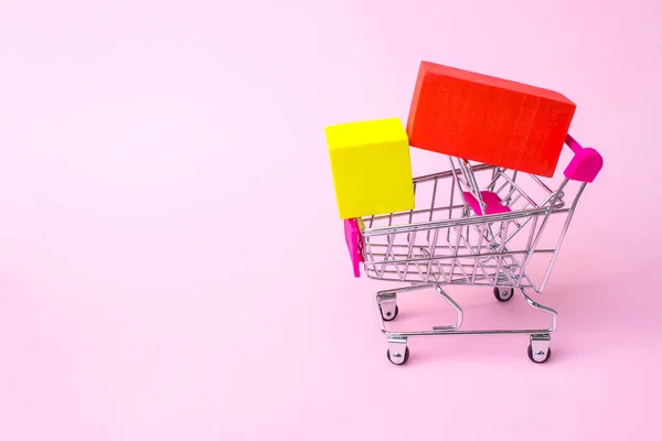 年間販売ショッピングシーズンコンセプト ピンクの背景に赤いプラスチックハンドル 赤と黄色のボックスでおもちゃの金属ショッピングカートを閉じます 大規模な販売と食料品の割引 食料品のための最高の価格 — ストック写真