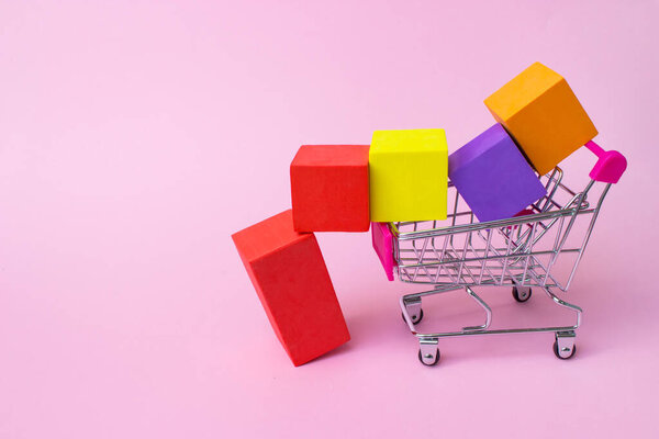 Colorful shopping cart with red plastic handle and multicolor boxes inside on pink background. Mock up header leave space for adding text or design for promote business campaign on line