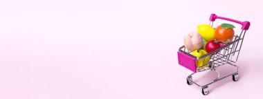 Mavi arka planda meyve ve sebzeli metal alışveriş arabası. Oyuncak minyatür alışveriş arabası