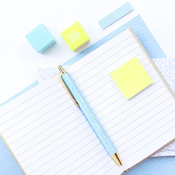 Office environment.  White desk with turquoise and yellow objects on a white table. Yellow notes, phone, notebook, pen.
