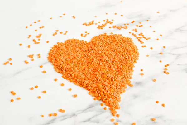 Heart drawn with red lentils on white marble.