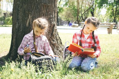 İki kız oturup bir ağaç doğa parkında yakınındaki okuyun.