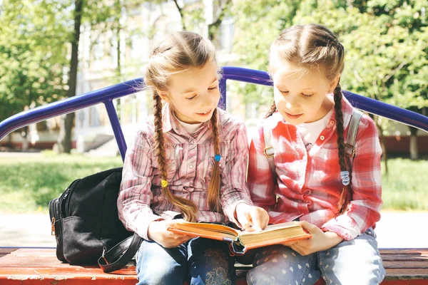 两个同学坐在长椅上读一本书 — 图库照片