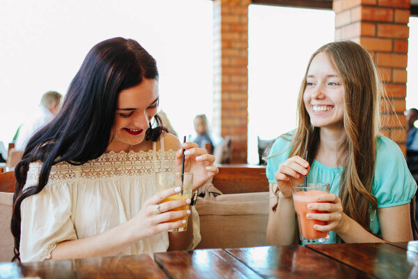 Two beautiful girls are drinking fresh fruit smoothies in a cafe.