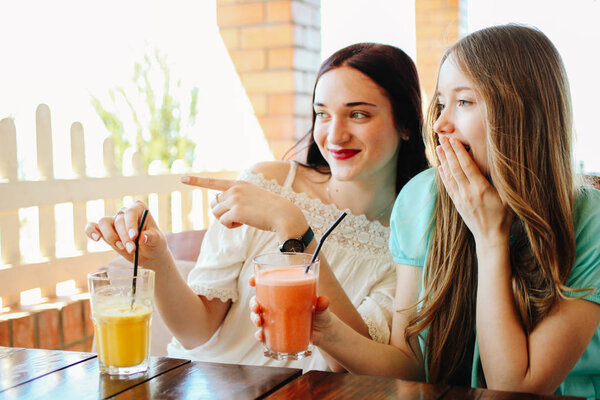 Two beautiful girls are drinking fresh fruit smoothies in a cafe.
