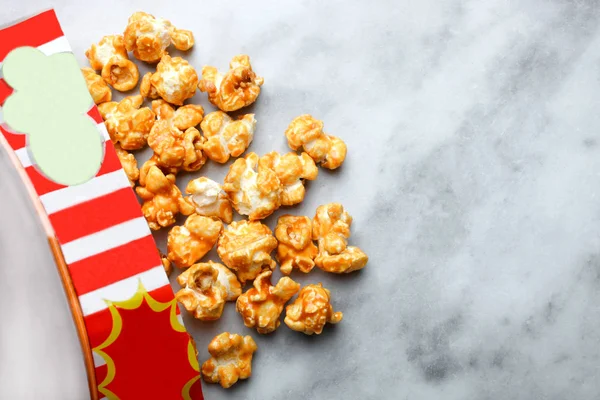 Sweet caramel popcorn in red packing on a marble background.