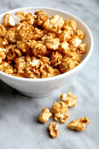 Sweet caramel popcorn in a white deep bowl on a marble background.