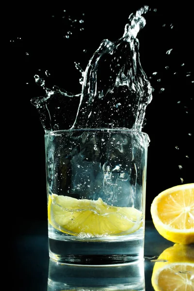 在水中的一片柠檬 在黑色的背景玻璃上 清凉的夏日饮品 — 图库照片