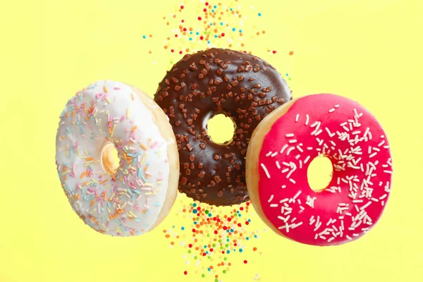 Three bright donuts with a powder on a yellow background.