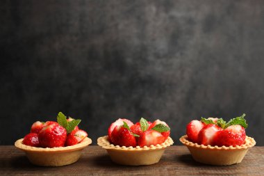 Siyah zemin ahşap bir masa üzerinde olgun çilek ile üç tartlets.