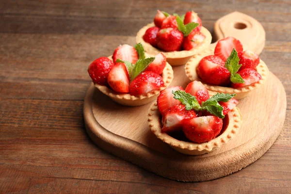 Tartlets ahşap arka plan üzerinde bir kesme tahtası üzerinde olgun çilek.