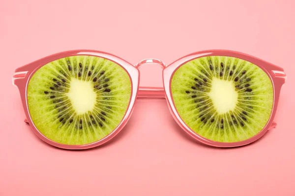 Bright pink sunglasses with kiwi on a pastel pink background.