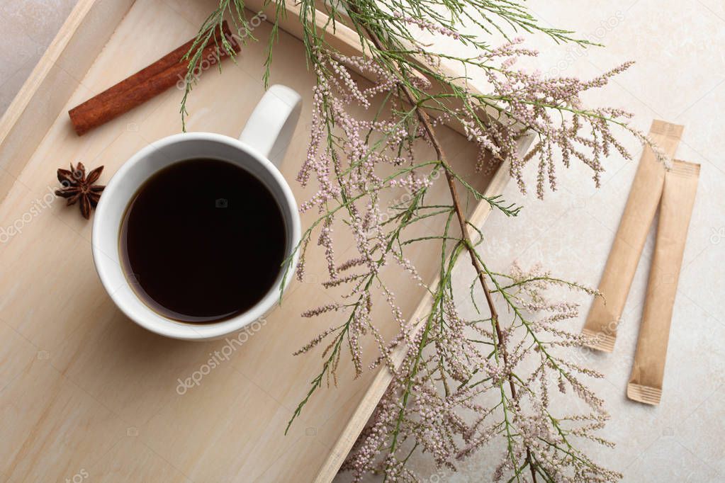 A cup of black tea stands on a wooden tray on a neutral background.