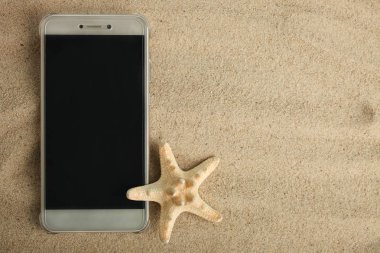 Modern bir akıllı telefon ve denizyıldızı sahil kumu yalan. Üstten görünüm.