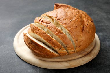 Bir kesme tahtası siyah bir arka plan üzerinde beyaz ekmek dilimlenmiş.