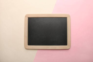 Siyah bir kara tahta bir pembe ve bej renkli arka plan üzerinde yatıyor. Üstten görünüm, kopya alanı.