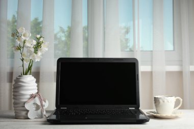 Dizüstü bilgisayar, kupa ve pencerenin önünde çiçek ile worktable.