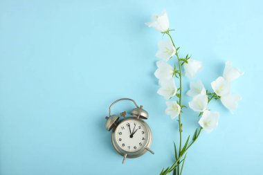 Güzel beyaz çiçekler çan ve mavi bir arka plan üzerinde bir çalar saat. Üstten görünüm.