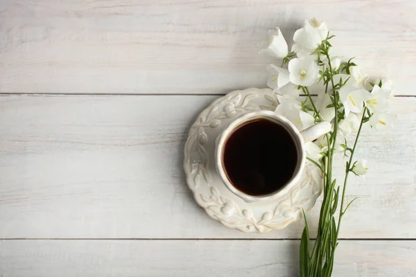 Beautiful bouquet of bells flowers and a cup of tea on a wooden background. Top view.