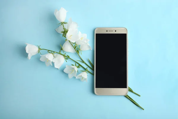 Güzel beyaz çiçekler çan ve mavi bir arka plan üzerinde modern bir akıllı telefon. Üstten görünüm.