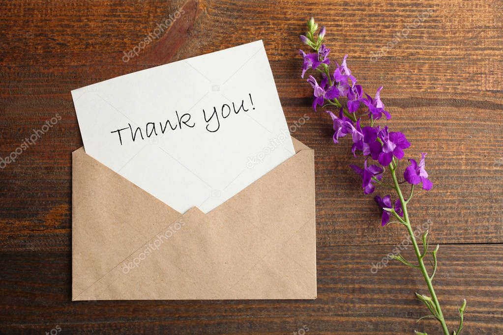 Envelope with a letter and a bouquet of purple flowers bells on a wooden background. Top view.