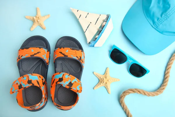 Children's summer sandals and a cap on a blue background, top view.