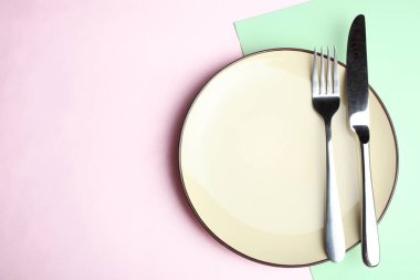 Tabak, çatal ve bıçak pembe ve yeşil bir arka plan üzerinde. Kavram sofra. Üstten görünüm