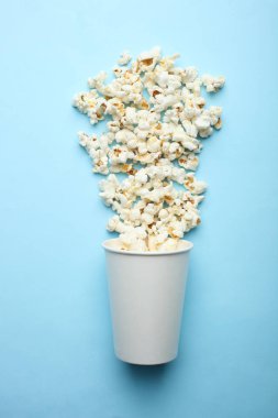 Tuzlu patlamış mısır ve pastel mavi bir arka plan üzerinde tek kullanımlık bir cam. Üstten görünüm.