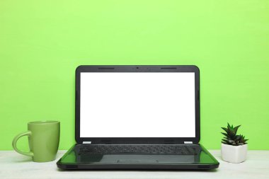 Laptop, a cup of tea and cactus on table on green background. Concept workplace. clipart