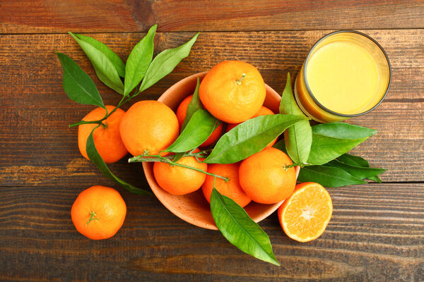 Bowl with bright and fresh tangerines and glass of juice on wooden background. Concept tangerine juice.