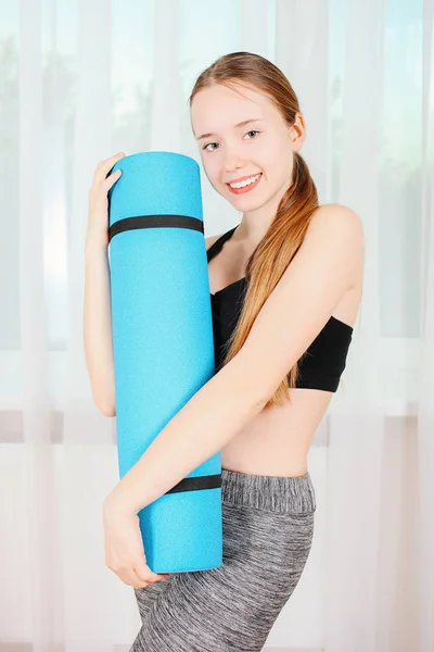 Girl with blue gym mat in front of window. Concept of sport.