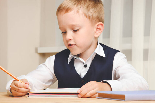 Schoolboy sits at desk and writes in notebook. Concept school.