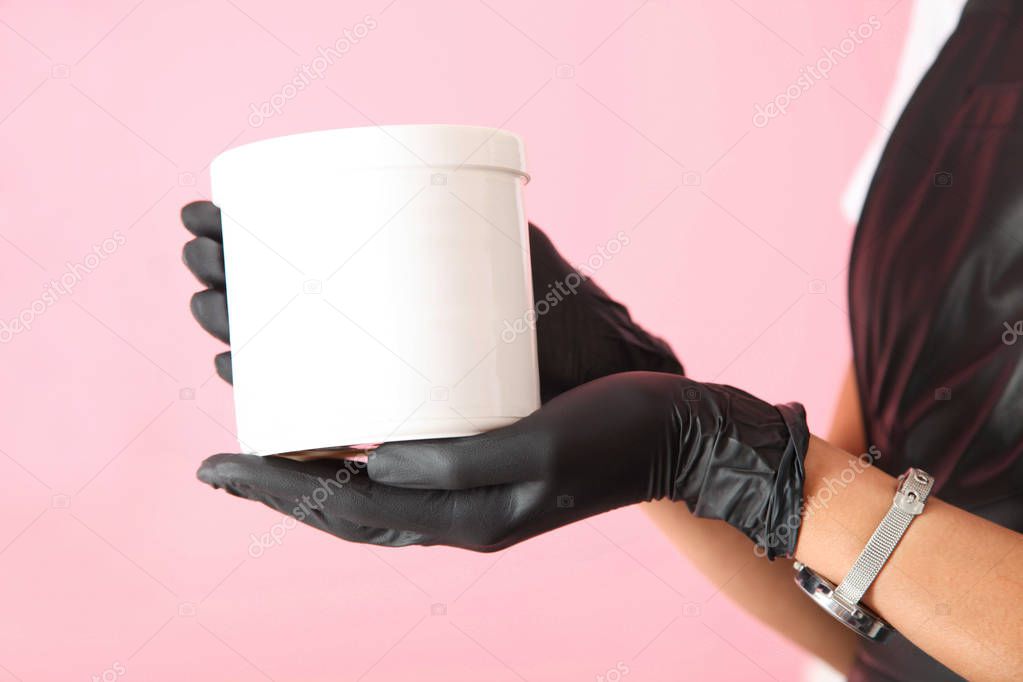 White container in hands on pink background. Concept skin care.