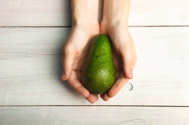 Olgun avokado ahşap arka plan üzerinde elinde. Üstten görünüm.